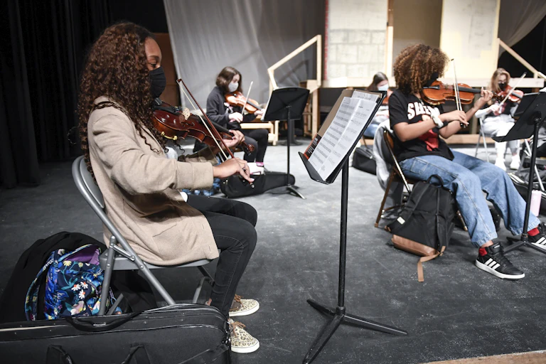 High schools students play violins while socially distanced and wearing face masks