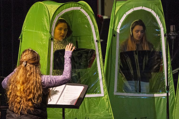 High school students sing in individual green tents during choir class