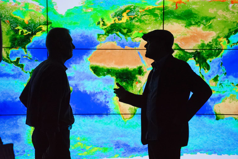 Two silhouetted figures stand in front of a world map.