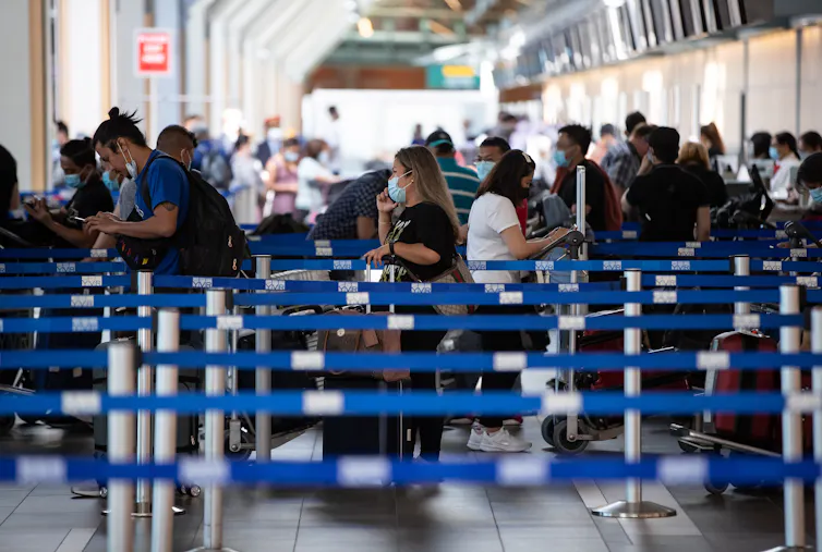 Travellers wearing face masks wait in line at an airport.