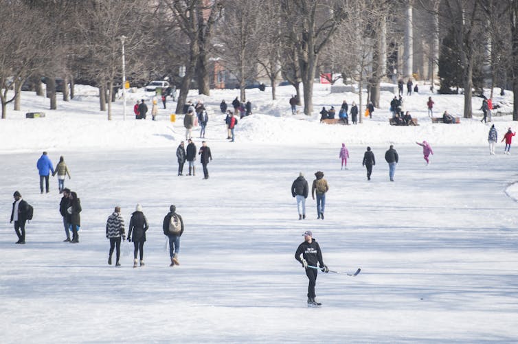 People walk and skate on a thawing lake in a park on a mild winter day in Montréal