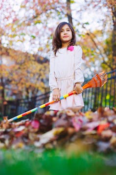 Girl standing in a pile of leaves holding a toy rake