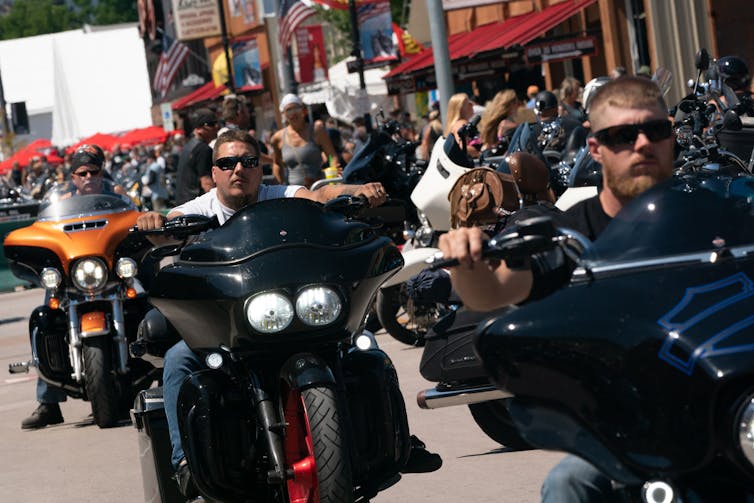 Unmasked motorcyclists crowd together.