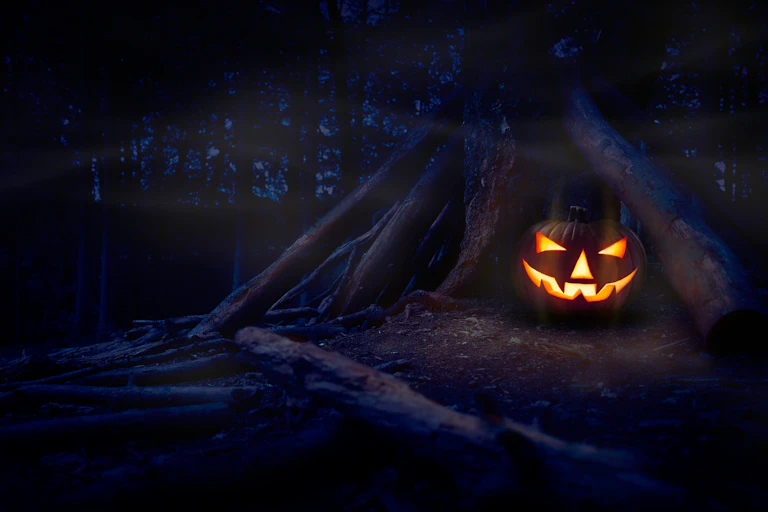 A jack o lantern seen in a forest setting.