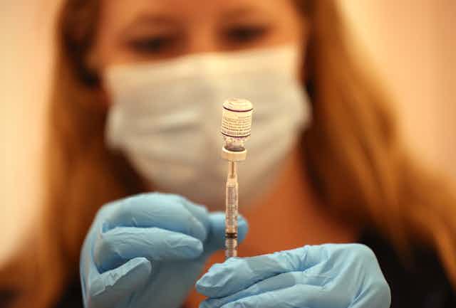 A female pharmacist fills a syringe with the Pfizer COVID-19 booster vaccine.