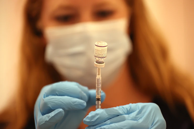 A female pharmacist fills a syringe with the Pfizer COVID-19 booster vaccine.