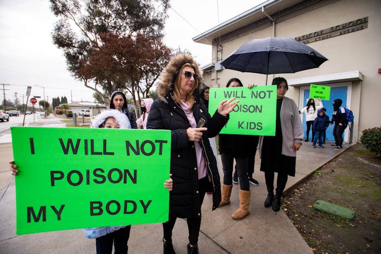 adults and kids with signs protesting COVID-19 vaccines