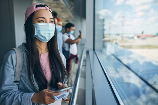 Young masked women holding passport looks out of airport building