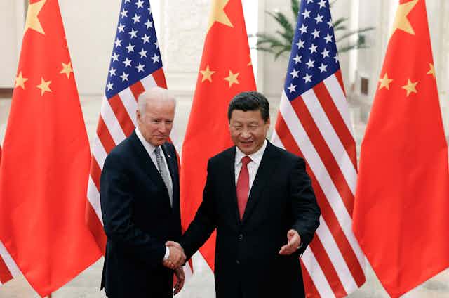 Joe Biden and Xi Jinping shake hands in front of China and US flags