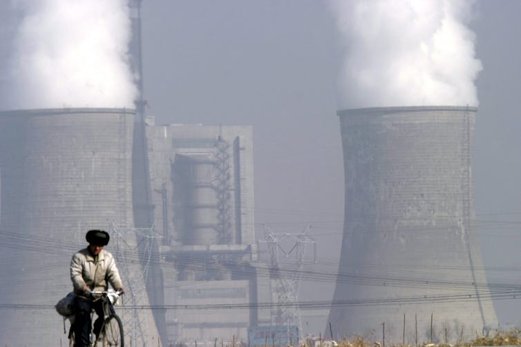 man rides bike past coal plant