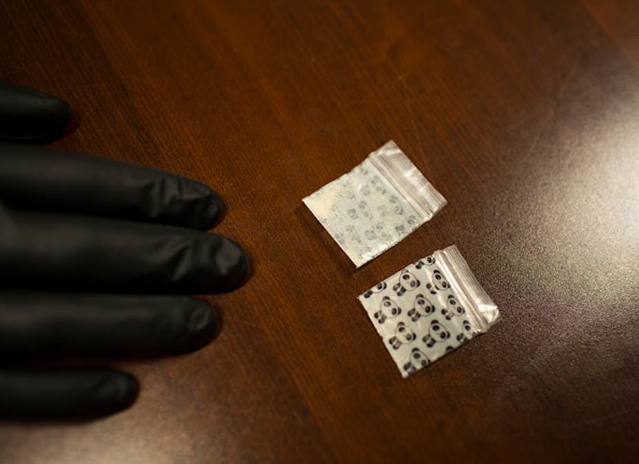 A hand wearing black gloves on a table with drugs on it.
