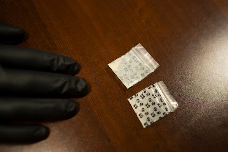 A hand wearing black gloves on a table with drugs on it.