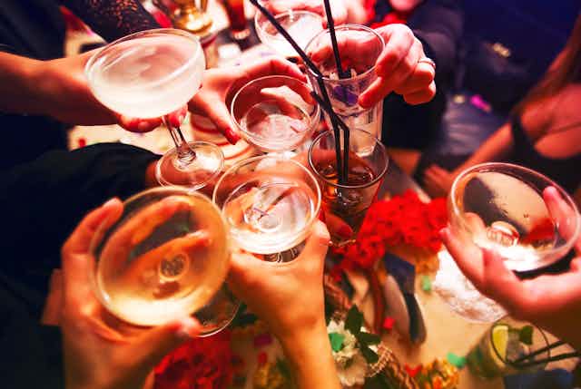 Close up on hands and glasses as people clink their alcoholic beverages together in a toast