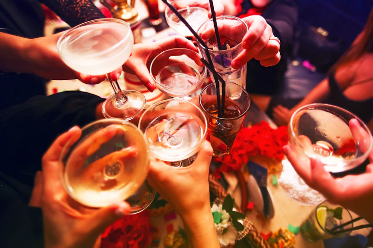 Close up on hands and glasses as people clink their alcoholic beverages together in a toast
