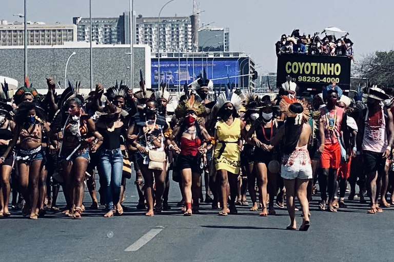 A group of protestors, some wearing regalia, stands in the street.