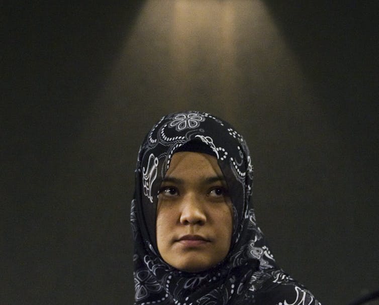 A woman wearing a hijab is pictured from the shoulders up, she is looking off into the distance