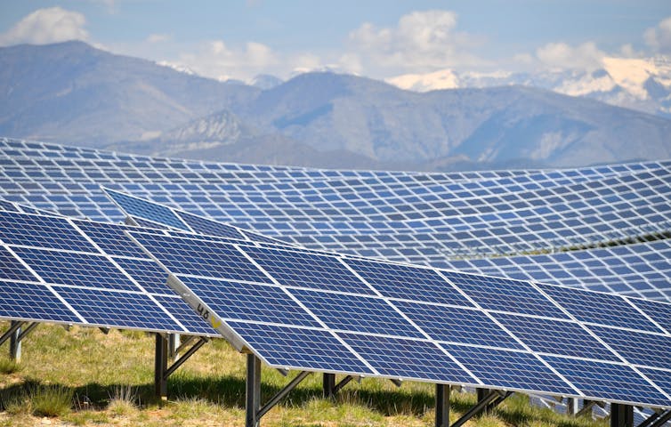 Rows of solar panels curve along a hillside with mountains in the background.
