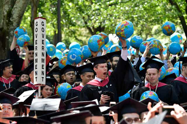 An assortment of students in black graduation caps and gowns hold up minature globes.