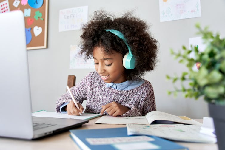 A girl wearing turquoise headphones studies online