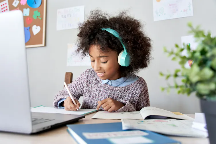 A girl wearing turquoise headphones studies online