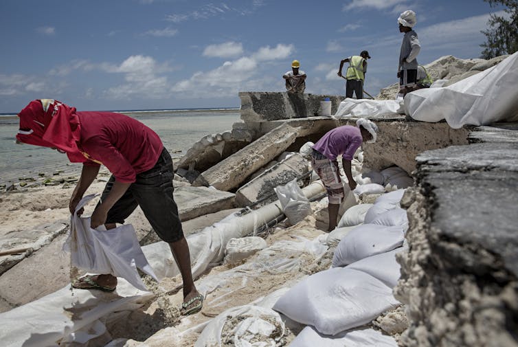 Men laying sandbags along a coastal road in Kiribati that was damaged by flooding related to sea level rise.