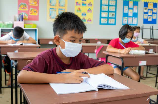 Boy wearing face mask works in notebook at school desk in classroom.