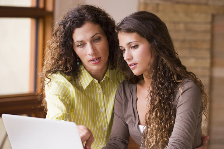 A mother and her daughter look on a laptop screen together.