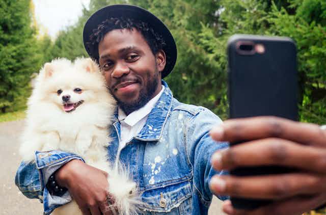A man wearing a hat takes a selfie while holding a Pomeranian