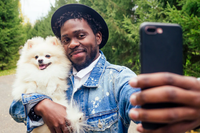 A man wearing a hat takes a selfie while holding a Pomeranian