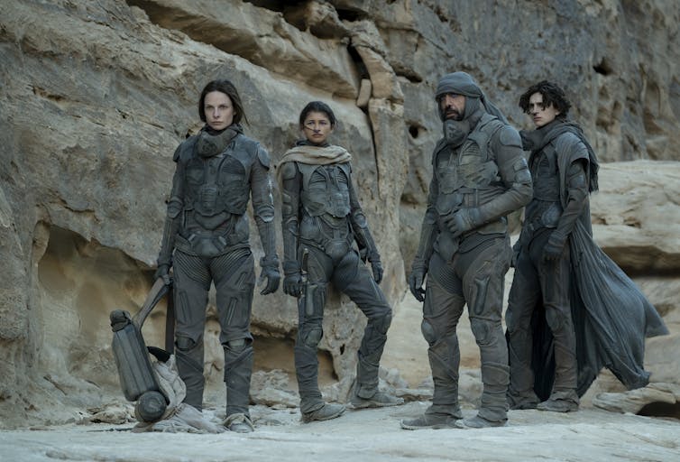 Four actors in black rubbery suits in desert from the Dune 2021 movie
