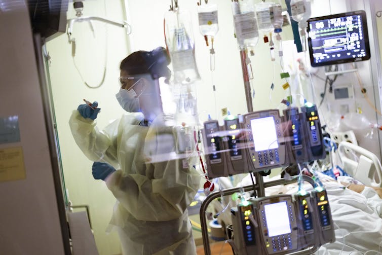 ICU worker in full PPE stands in front of monitor.