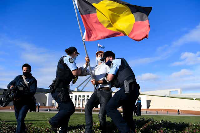 Police wrestle with protester bearing Aboriginal flag outside Parliament House in Canberra