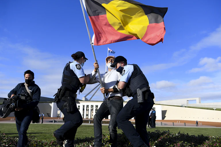 Police wrestle with protester bearing Aboriginal flag outside Parliament House in Canberra