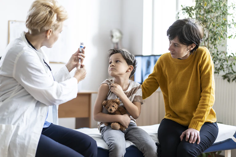 Little boy with teddy bear getting vaccinated at doctor's office.