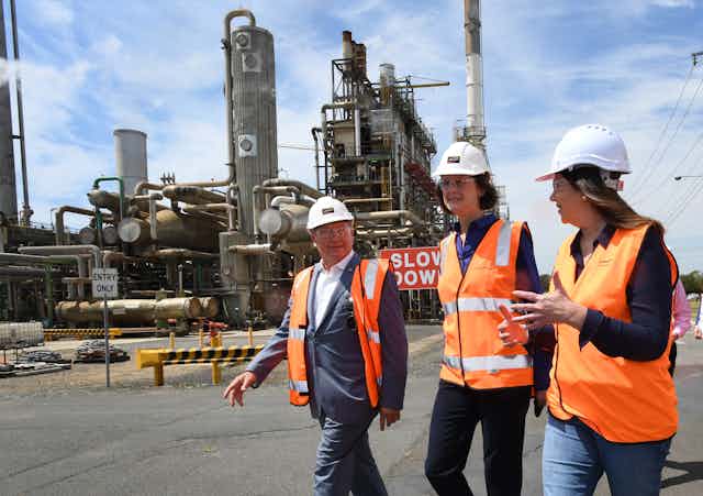 man and two women walk in front of industrial site