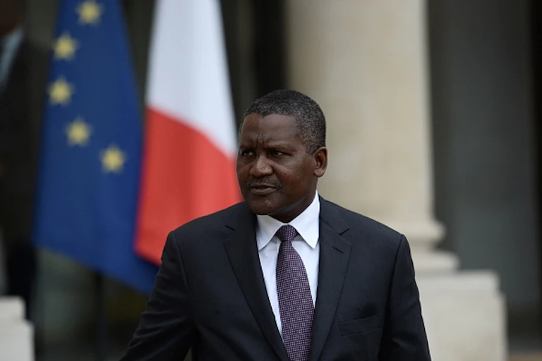 Head and shoulders of a man in a suit and tie, with flags in the background