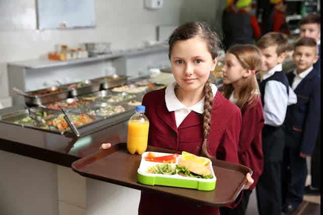 A girl holds a tray of lunch in a canteen.