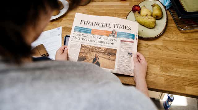 A person reads a headline about climate change in the Financial Times.