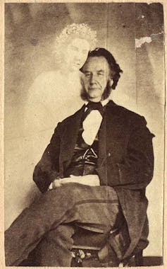 Photograph of a seated man with a semi-translucent female figure standing next to him.