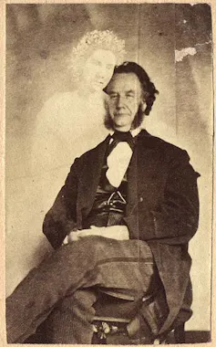 Photograph of a seated man with a semi-translucent female figure standing next to him.