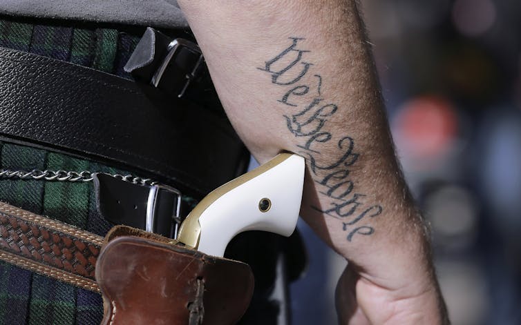 A man with a tattoo that reads 'We the People' carrying a gun in a leather holster