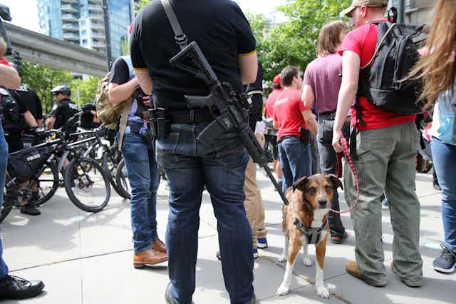 A man carrying an automatic rifle at an open carry rally on a sidewalk 
