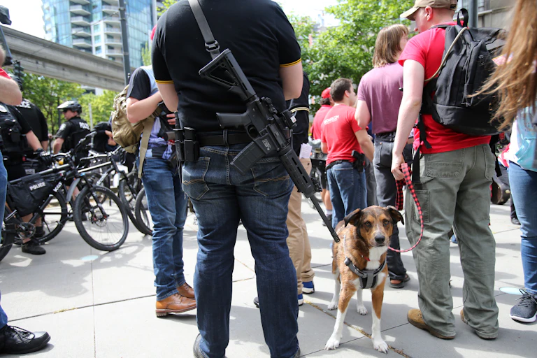 A man carrying an automatic rifle at an open carry rally on a sidewalk