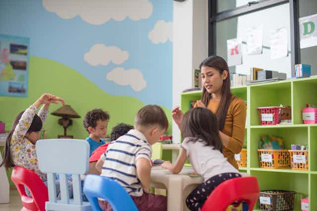 Early childhood teacher watches over children taking part in an activity at a table