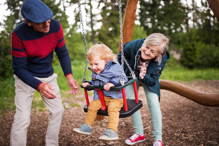 Grandparents push a grandchild on a swing.