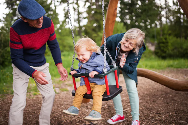 Grandparents push a grandchild on a swing.