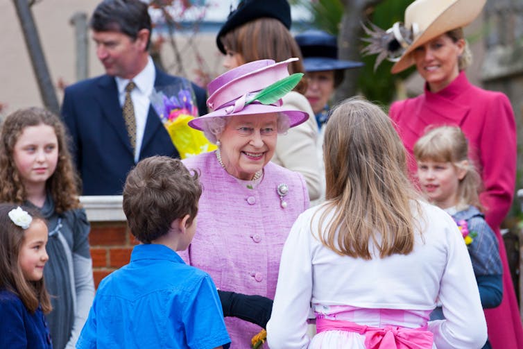 The Queen smiles at children surrounding her.