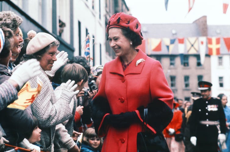The Queen smiles as she walks past a line of people clapping.