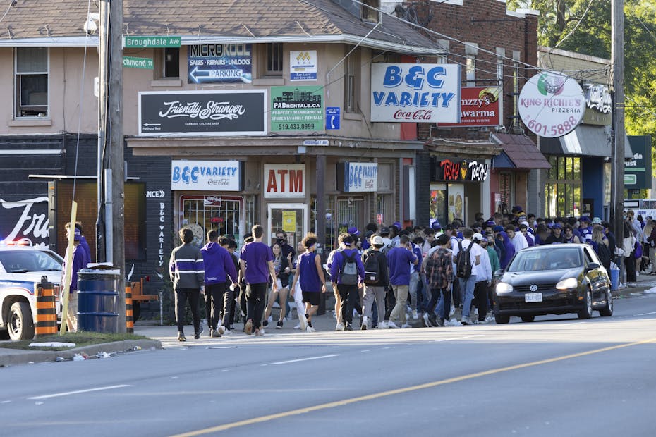 A group of students wearing purple walk down a street in London, Ont.