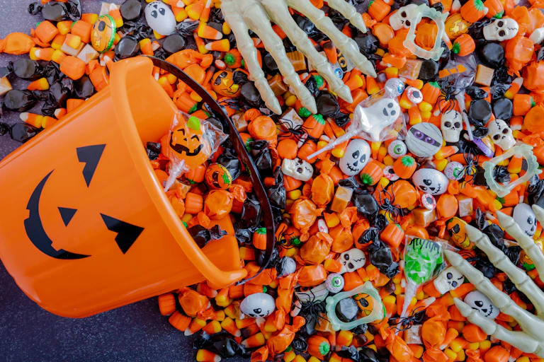 A jack o lantern bucket with candy spilling out and skeleton hands sorting it.